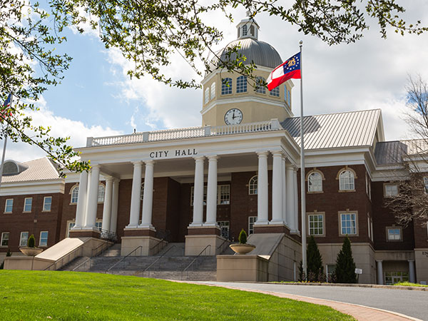 Front-facing view of Roswell city hall on a bright sunny day with the Georgia flag blowing in the wind